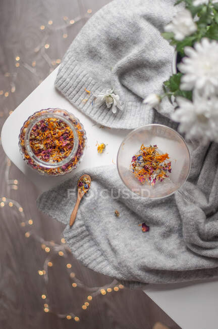 Une tasse en verre avec thé de fleur sec et un bocal sur un pull gris. — Photo de stock