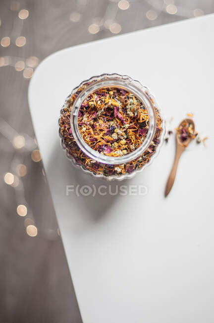 Стеклянная банка с сухим цветочным чаем и деревянная ложка против огней — стоковое фото