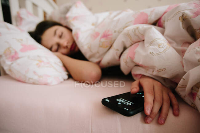 Menina dormindo em uma cama e segurando seu telefone — Fotografia de Stock