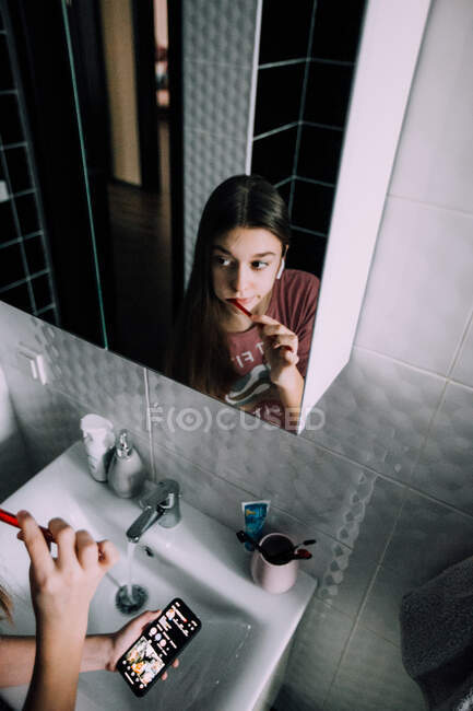 Chica cepillándose los dientes y sosteniendo su teléfono - foto de stock