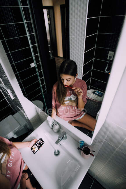 Mädchen putzt sich die Zähne und schaut aufs Handy — Stockfoto