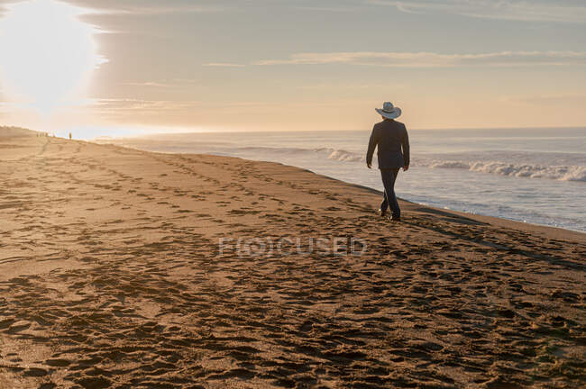 Mann spaziert mit Hut im Sonnenuntergang am Strand — Stockfoto