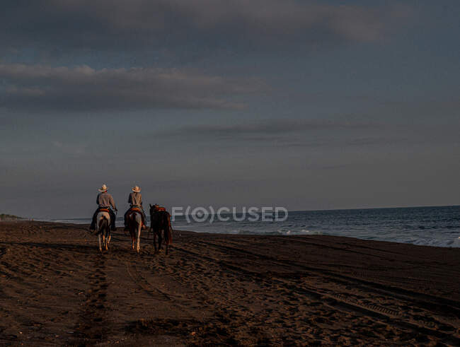 Uomini a cavallo sulla spiaggia al tramonto — Foto stock