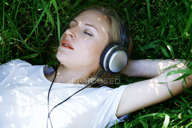 Frau mit Kopfhörer liegt im Gras — Stockfoto