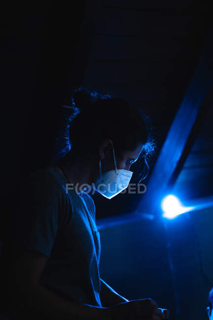 Jovem trabalhando com uma máscara de proteção e ligth azul atrás — Fotografia de Stock