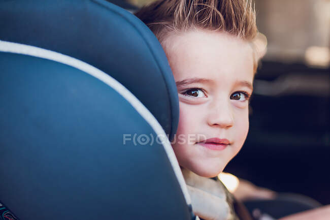 Junge im Vorschulalter sitzt im Autositz im Auto und schaut in die Kamera. — Stockfoto
