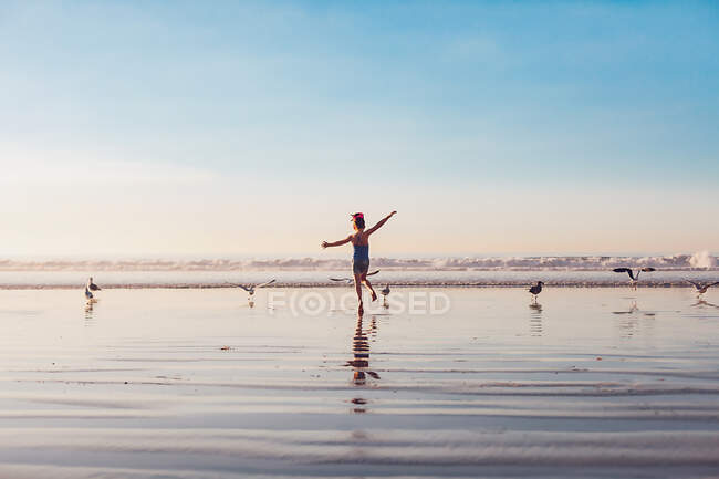 Fille courir avec des oiseaux à la plage à l'heure d'or. — Photo de stock