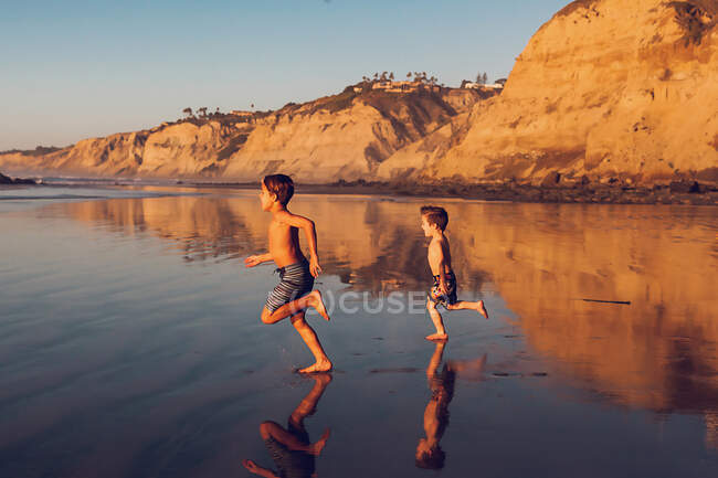 Два хлопці біжать на пляжі при заході сонця.. — стокове фото