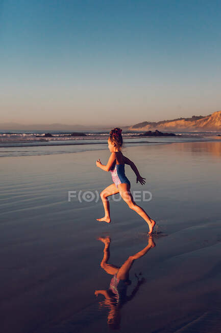 Escola menina envelhecida correndo em direção à água na praia. — Fotografia de Stock