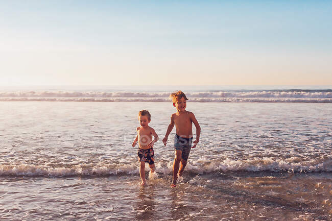 Dois meninos correndo na água na praia. — Fotografia de Stock
