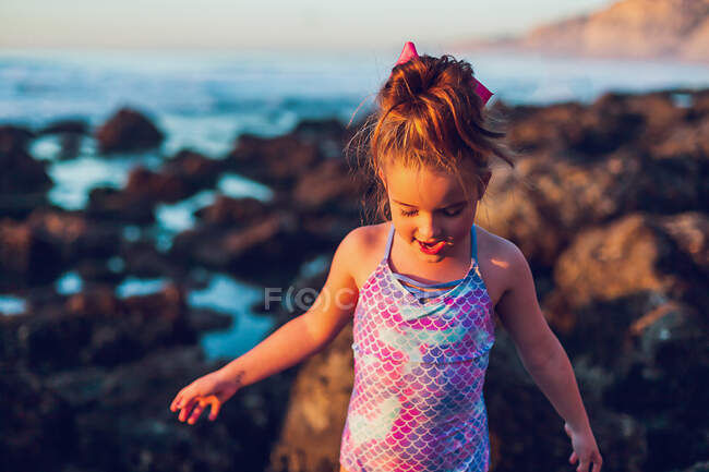 Chica caminando sobre rocas en la playa a la hora dorada. - foto de stock