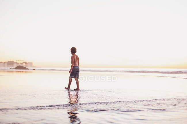 Jeune garçon au coucher du soleil sur la plage — Photo de stock