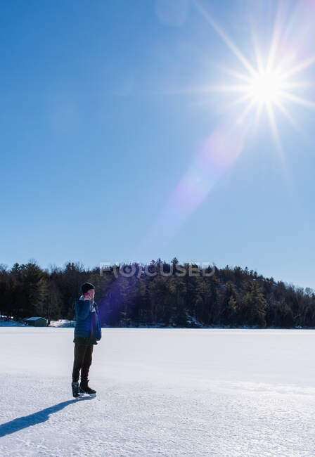 Мальчик-подросток на смартфоне и катается на коньках по замерзшему озеру в зимний день. — стоковое фото