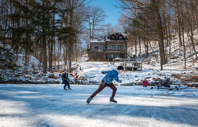 Дети катаются на коньках на открытом катке на замерзшем озере за коттеджем. — стоковое фото