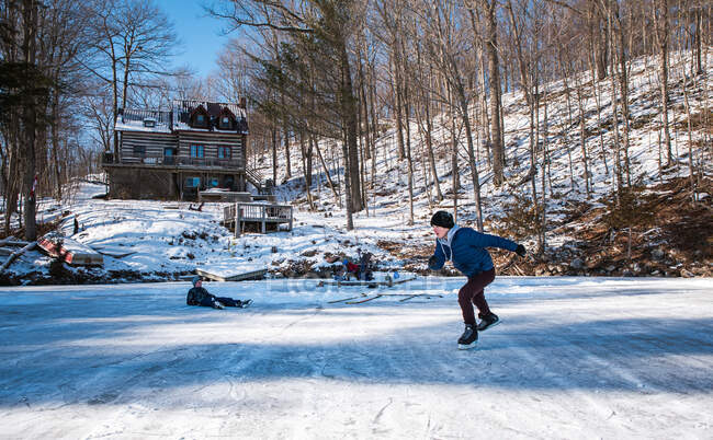 Kinder beim Schlittschuhlaufen auf einer Eisbahn am zugefrorenen See hinter einer Hütte. — Stockfoto