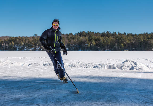 Ragazzo adolescente che gioca a hockey su una pista all'aperto su un lago ghiacciato in Canada. — Foto stock