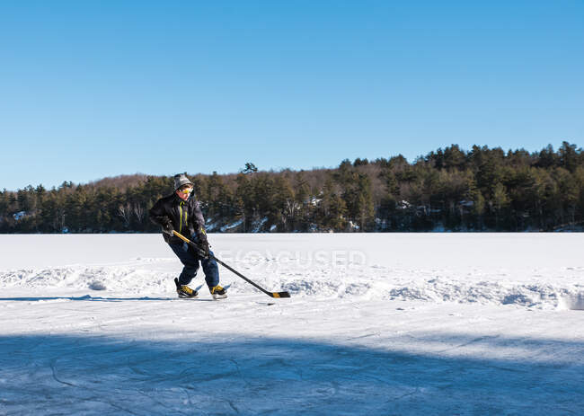 Teenie-Junge spielt Hockey auf einer Eisbahn an einem zugefrorenen See in Kanada. — Stockfoto