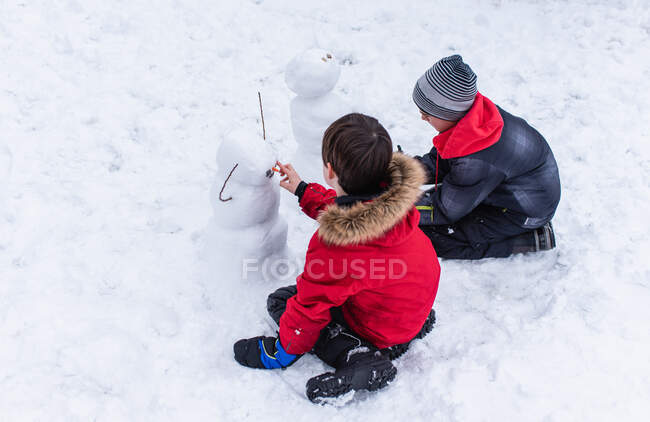 Два мальчика в зимней одежде строят снеговиков в зимний день. — стоковое фото