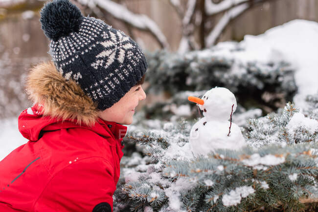 El niño con muñeco de nieve en un bosque cubierto de nieve - foto de stock