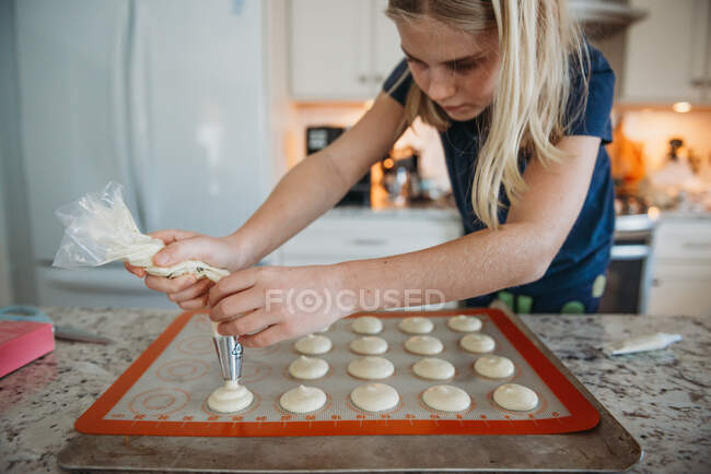 Close up de mãos de menina jovem tubulação de macarons na cozinha — Fotografia de Stock