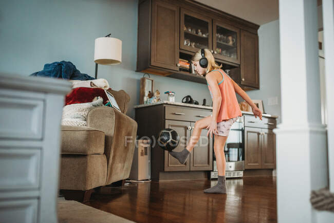 Young girl balancing soccer ball on foot indoors watching iPad — Stock Photo