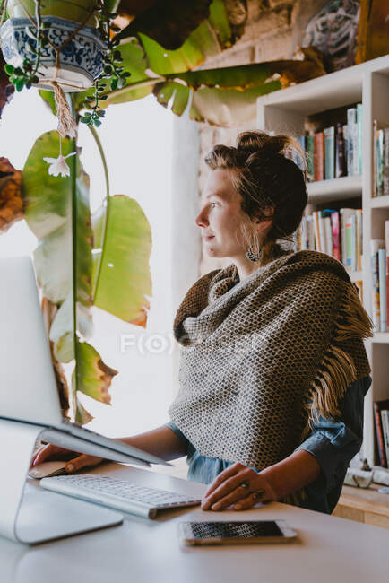 Стильна жінка працює на ноутбуці з домашнього офісу в оточенні рослин — стокове фото