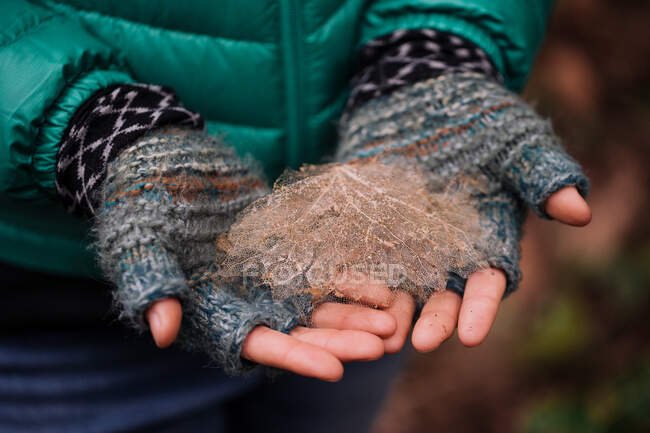 Donna tiene su una foglia morta che indossa guanti in inverno — Foto stock
