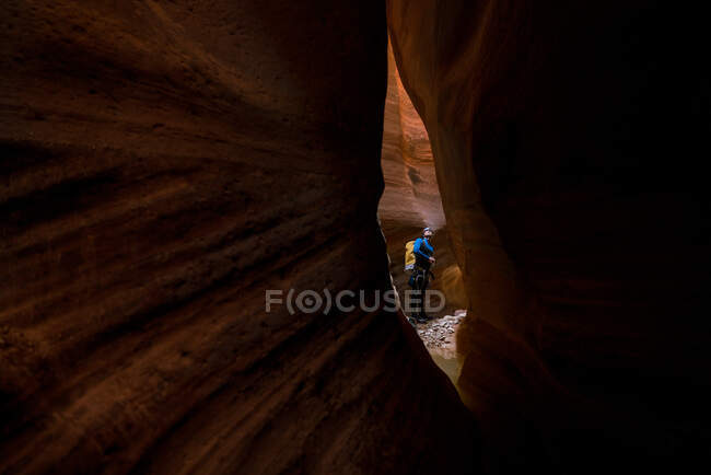 Un homme est vu à travers une petite fente de roche rouge à l'intérieur d'un canyon — Photo de stock