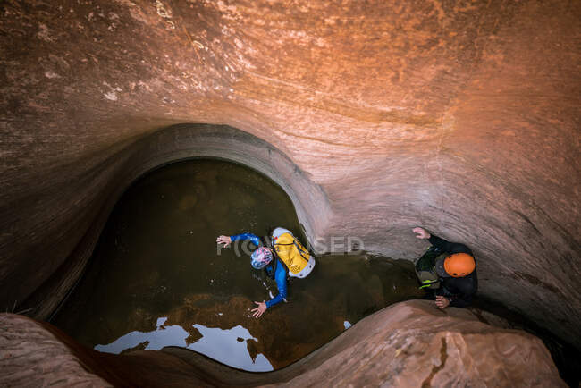 Two men wade through chest deep water to navigate a slot canyon — Stock Photo