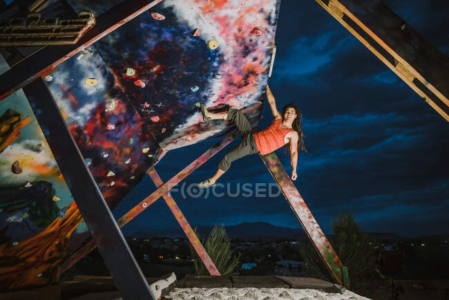 A young male climber hangs out on an outdoor climbing wall at night — Stock Photo