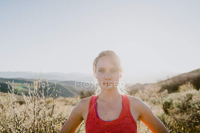 Femme blonde athlétique vous regarde avec le soleil et les montagnes derrière — Photo de stock