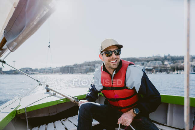 Красивий молодий чоловік посміхається і пливе маленьким човном у сонячний день — стокове фото
