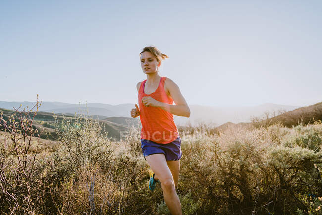 Athletic blonde woman trail runs in the mountains at golden hour — Stock Photo
