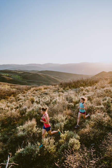 Two athletic women trail run in the mountains at golden hour — Stock Photo