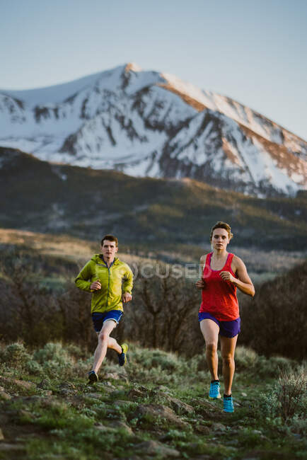 A woman and man trail run at sunset with snowy peak in the distance — Stock Photo
