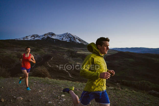 Молодий чоловік і жінка біжать сутінками з гірським видом. — стокове фото