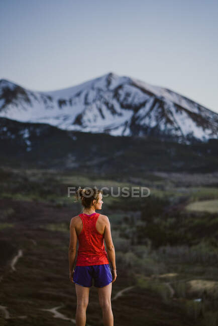 Jovem mulher olha para as montanhas enquanto trilha correndo ao entardecer — Fotografia de Stock