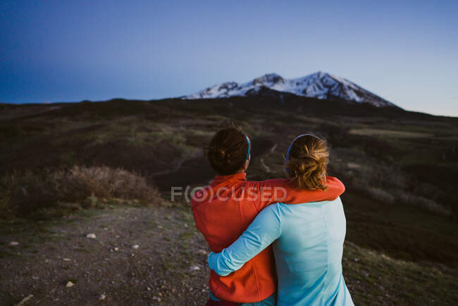 Две подруги обнимаются и смотрят на горы в сумерках — стоковое фото