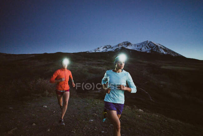Two women run at night in the mountains wearing headlamps — Stock Photo