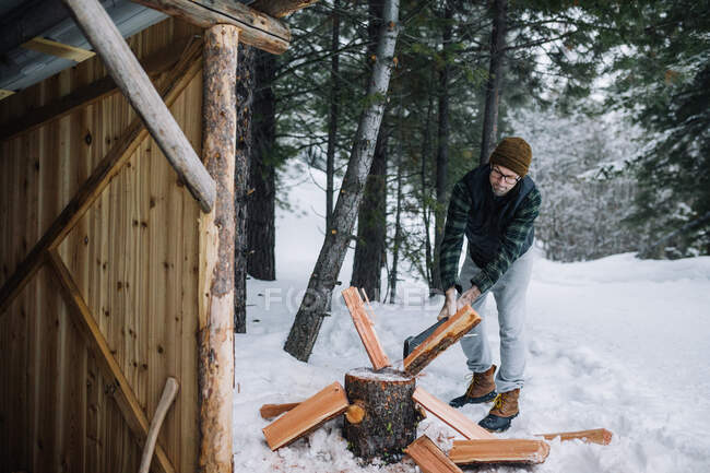Мужчина в фланелевой рубашке рубит дрова на улице в снегу — стоковое фото