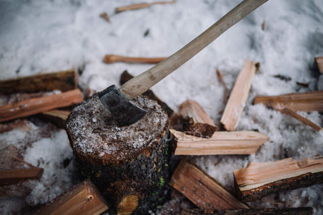 Un hacha de madera manejada se pega en un tronco con leña y nieve a su alrededor - foto de stock