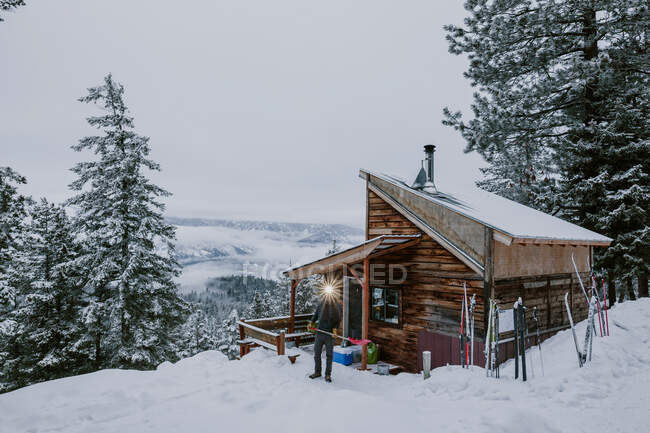 Um homem com pás de farol neve na frente da cabine e vista para a montanha — Fotografia de Stock
