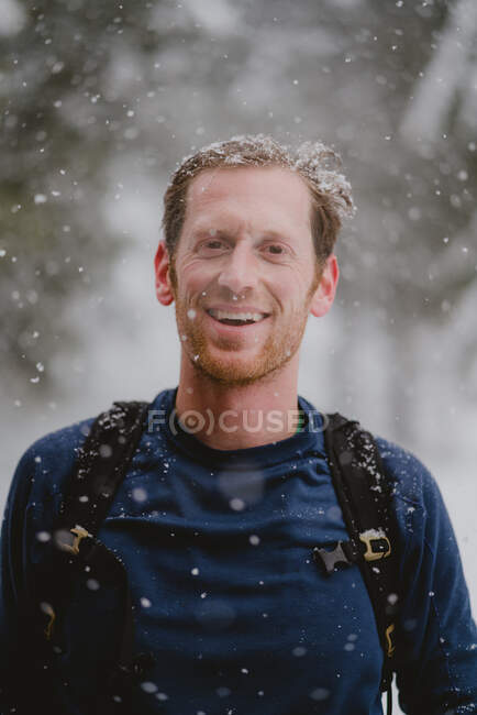 Retrato del hombre con mochila sonriendo con nieve en el pelo - foto de stock