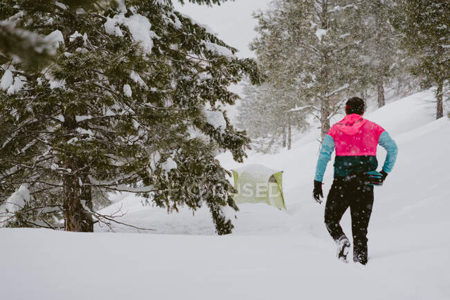 Un uomo in giacca luminosa cammina attraverso la neve profonda fuori dalla sua tenda — Foto stock
