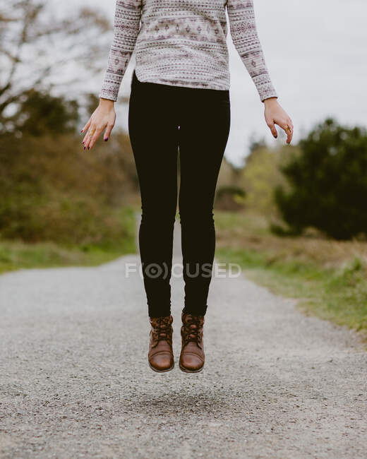 Eine Frau mit Lederstiefeln springt auf einem Schotterweg in die Luft — Stockfoto