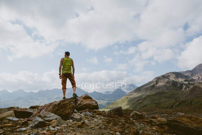Um homem em pé no cume rochoso olha para a vista da montanha — Fotografia de Stock