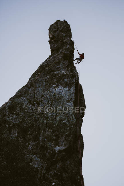 Eine Bergsteiger-Silhouette seilt sich in der Abenddämmerung von einem schmalen Gipfel ab — Stockfoto