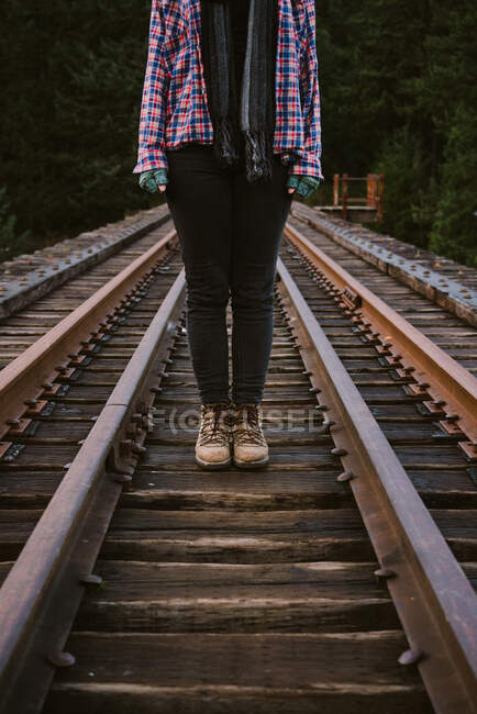 Woman in leather boots and flannel stands on railroad tracks — Stock Photo