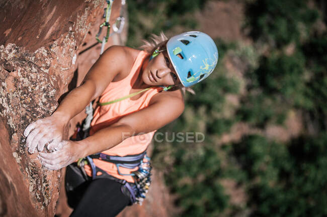 Mujer escaladora se aferra a las rocas con las manos con tiza en lo alto de la pared - foto de stock