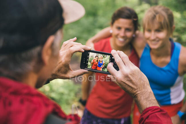 Drei Freunde, die zusammen laufen, bleiben stehen, um ein Foto mit dem Smartphone zu machen — Stockfoto